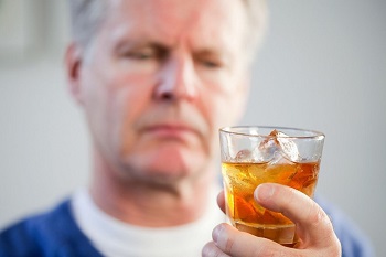 Мужчина смотрит на стакан с алкоголем